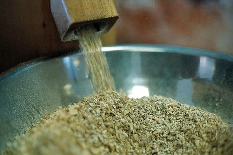 Grains pouring from a wooden chute into a metal bowl.