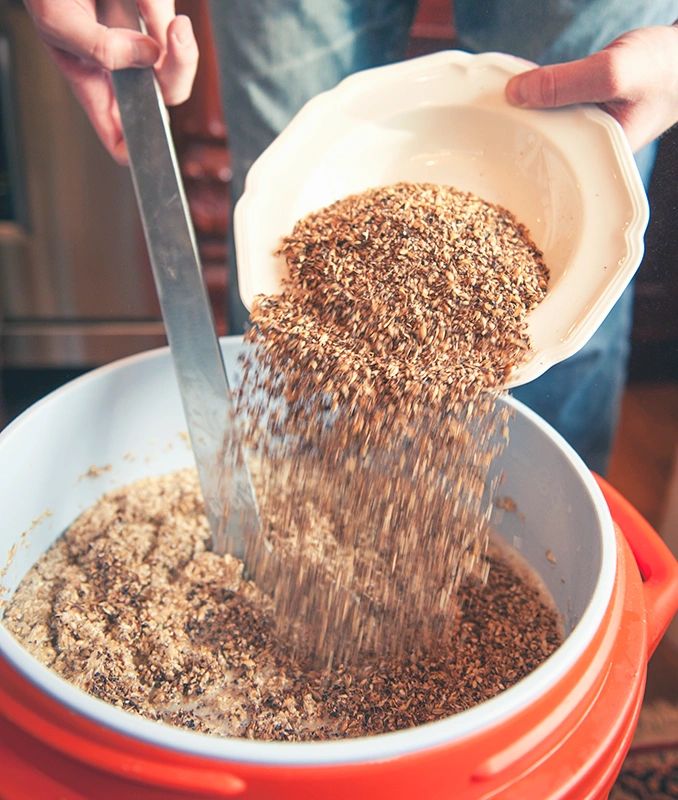 Person pouring grains into a large container for mixing.