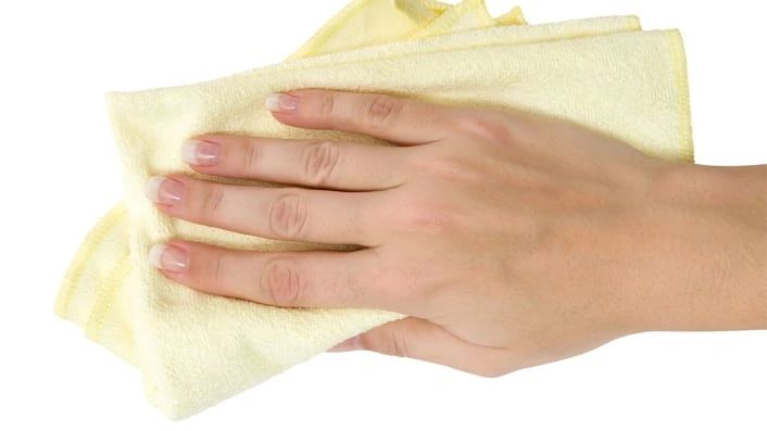 Hand holding a yellow cleaning cloth against a white background.